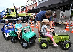 Drei Kinder fahren auf drei kleinen Spielzeug-Nutzfahrzeugen