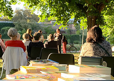 Lesung im Freien vor Publikum, im Vordergrund ein Tisch mit Büchern