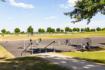 Mehrere Personen spielen auf dem Hartplatz im Sport- und Freizeitpark Wiley Basketball und Fußball.