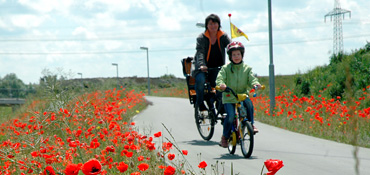 Frau mit kleinem Jungen beim Radfahren, ringsherum am Radwegrand blüht roter Klatschmohn