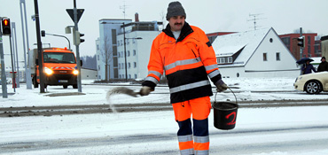 Mitarbeiter des Bauhofes streut Streugut auf die schneebedeckte Fahrbahn