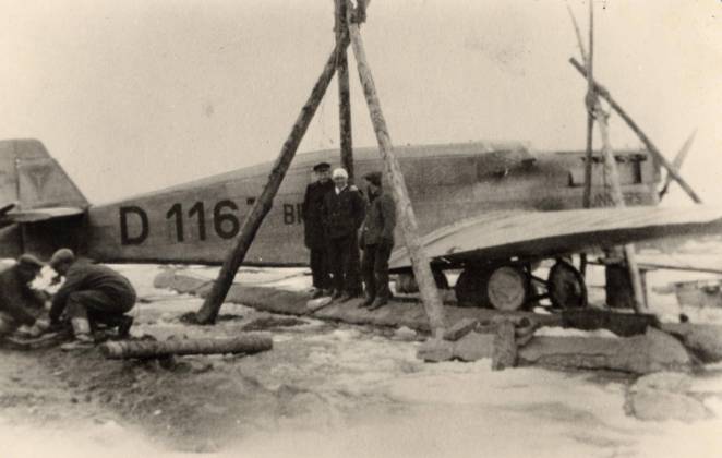 Schwarz-Weiß-Foto: Drei Männer stehen vor einem Flugzeug
