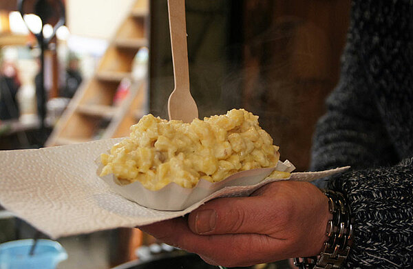 Jemand hält eine Schachtel mit einer Portion Käsespätzle in der Hand