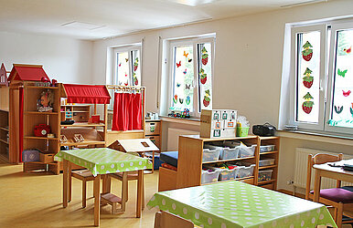 Kita-Gruppenraum mit Tischen sowie Bastel- und Spielbereich
