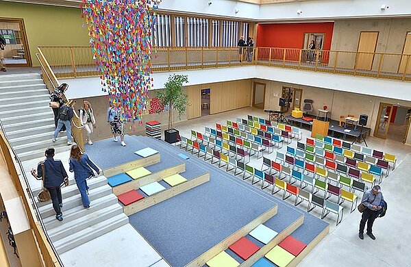 Blick von oben in die offene Aula mit Sitzstufen mit bunten Kissen