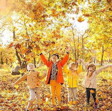 Kinder spielen im bunten Herbstlaub und werfen Blätter in die Luft.