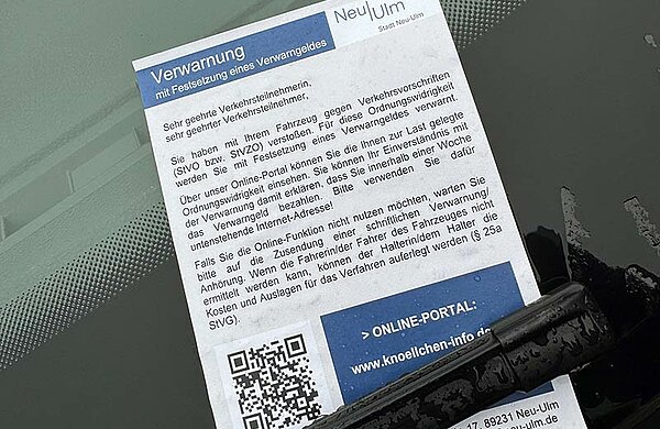 Zettel an der Windschutzscheibe eines Autos mit Beschriftung "Verwarnung" und einem QR-Code