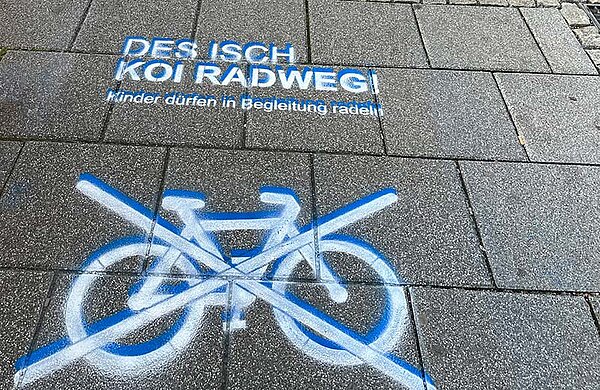 Eine Markierung auf dem Gehweg mit einem durchgestrichenen Fahrrad und darüber dem Text: Des isch koi Radweg!