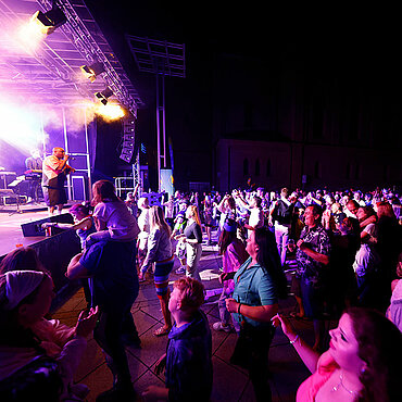 Stadtfest-Besucher feiern und tanzen vor einer Bühne, auf der eine Band spielt