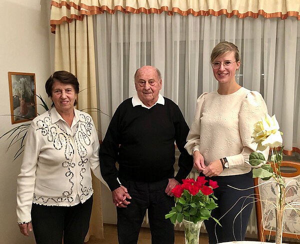 Oberbürgermeisterin Katrin Albsteiger steht neben den Eheleuten in deren Wohnzimmer. Alle drei lächeln in die Kamera.