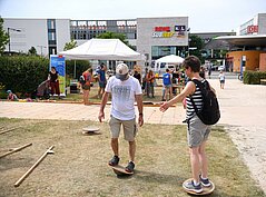 Zwei Personen balancieren auf Sportgeräten, im Hintergrund der Neu-Ulmer Bahnhof