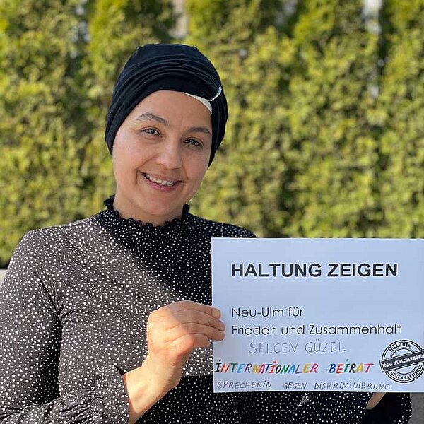 Eine junge Frau hält ein Blatt in die Kamera mit der Aufschrift: Haltung zeigen. Neu-Ulm für Frieden und Zusammenhalt.
