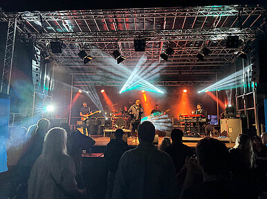 Eine Band spielt nachts auf einer beleuchteten Bühne vor Publikum