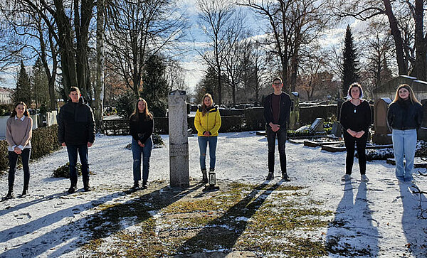 Sieben Jugendliche stehen neben dem Gedenkstein für jüdische Mitbürger auf dem Neu-Ulmer Friedhof.
