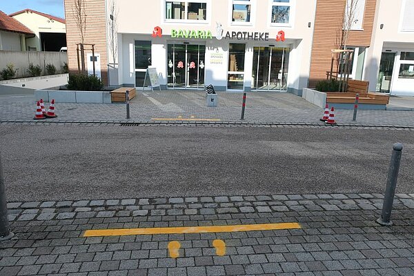 Gelbe Markierungen an einer Straße. Die Markierung zeigt einen Querbalken mit dahinter liegenden Fußabdrücken.