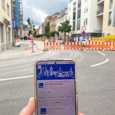 Smartphone mit Hinweis "Bauvorhaben Innenstadt" und der Neu-Ulmer Skyline, im Hintergrund eine Baustelle in der Neu-Ulmer Schützenstraße
