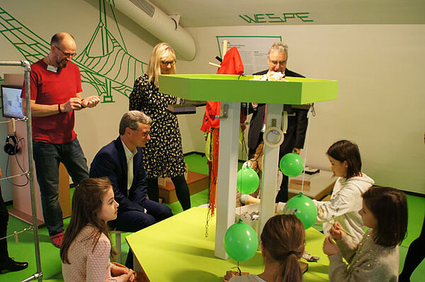 Mehrere Kinder erkunden eine Mitmachstation im Kindermuseum, Staatsminister Bernd Sibler, Neu-Ulms Oberbürgermeister Gerold Noerenberg und weitere Personen sitzen und stehen darum.