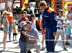 Ein kleines Mädchen hält bei der Spielstation der Feuerwehr einen Feuerwehrschlauch in der Hand