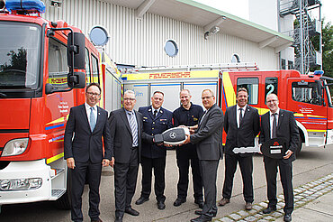 Oberbürgermeister Gerold Noerenberg sowie Vertreter von Feuerwehr, Mercedes-Benz und Magirus vor den beiden neuen Feuerwehrfahrzeugen. Zwei große symbolische Schlüssel werden in den Händen gehalten.