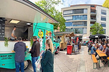 Marktgeschehen auf dem Petrusplatz in Neu-Ulm mit Besucherinnen und Besuchern an Gastronomieständen und Biertischen.