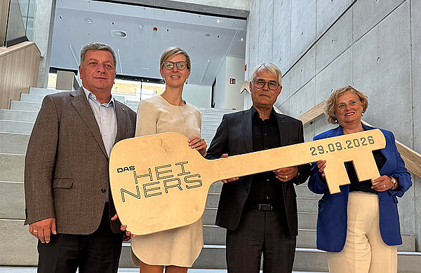 Vertreter von Stadt, Ministerium und beteiligten Partnern halten bei der Übergabe einen symbolischen großen Schlüssel mit der Aufschrift "Das Heiners".