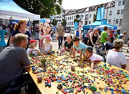 Kinder und Erwachsene rund um einen Tisch voller Legosteine