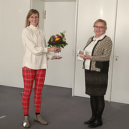 Brigitte Weiss hält die Ehrenmedaille für Pflege in die Kamera, Oberbürgermeisterin Katrin Albsteiger überreicht ihr einen Blumenstrauß.