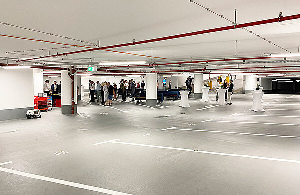 Parkplätze in der Tiefgarage, im Hintergrund Personen an Stehtischen