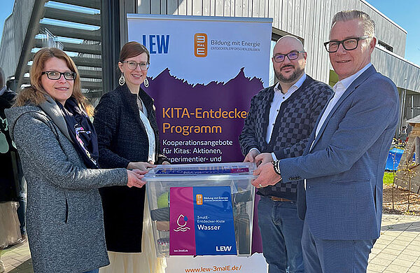 Übergabe der Entdecker-Kiste an das Kinderhaus Abenteuerland Vier Personen halten eine Kiste mit der Aufschrift "Entdecker-Kiste Wasser"