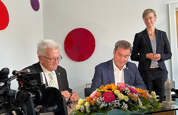 Die beiden Ministerpräsidenten sitzend an einem Tisch mit Blumenschmuck, hinter ihnen steht Oberbürgermeisterin Katrin Albsteiger