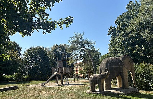 Grünfläche mit großen Skulpturen in Form von Elefanten sowie einem Spielplatz