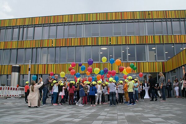 Das Schulgebäude der neuen Mark-Twain-Grundschule in Neu-Ulm mit ihren markanten bunten Fassade, im Hof vor dem Gebäude tummeln sich die Erstklässler mit bunten Luftballons in der Hand