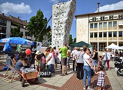 Besucher von "Neu-Ulm spielt" stehen rund um die mobile Kletterwand auf dem Neu-Ulmer Rathausplatz