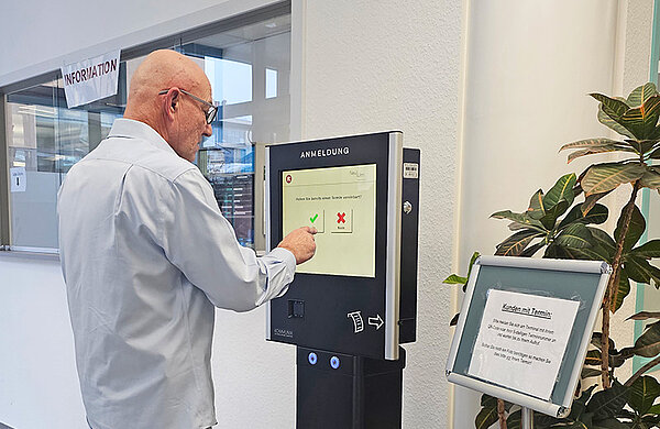 Eine Person bedient das digitale Anmeldeterminal.