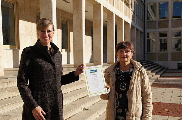 Oberbürgermeisterin Katrin Albsteiger und Ute Seibt halten die Urkunde zur Rezertifizierung der Stadt Neu-Ulm als Fairtrade-Stadt in Händen.
