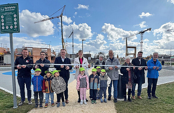 Mehrere Personen der Stadt und Baufirma durchschneiden ein symbolisches Band vor dem neuen Spielplatz Illerpark, vor ihnen stehen Kinder.