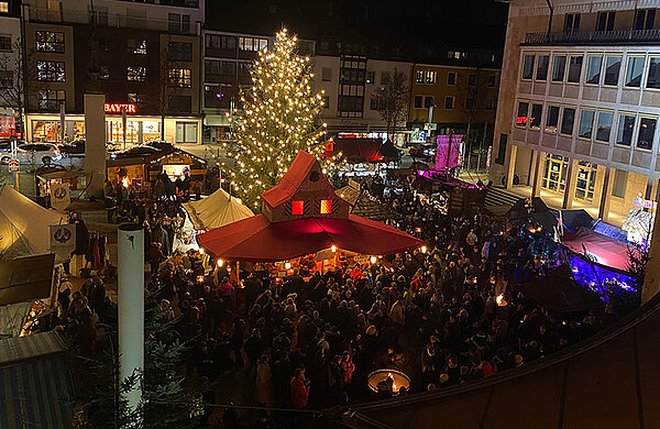 Blick von oben auf den Weihnachtsmarkt auf dem Neu-Ulmer Rathausplatz mit beleuchtetem Weihnachtsbaum und Besuchern