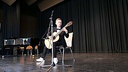 Ein Junge sitzt vor einem Mikrophon und spielt Gitarre