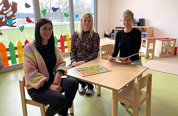 Oberbürgermeisterin Katrin Albsteiger und die beiden Mitarbeiterinnen der Kita sitzen an einem Tisch im Gruppenraum der Kita Abenteuerland.