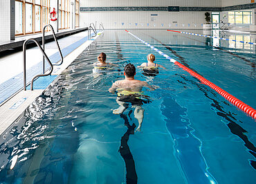 Drei Personen beim Aquajogging in einem Schwimmerbecken im Hallenbad.