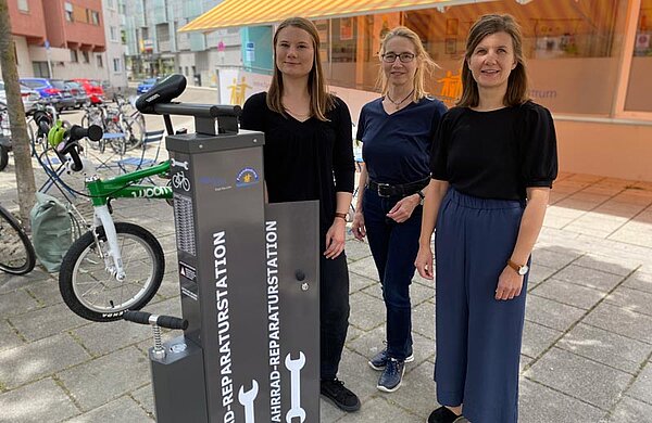 Die drei genannten Personen stehen neben der Fahrrad-Reparaturstation vor dem Familienzentrum