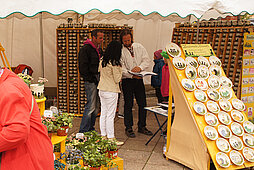 Marktbesucher an einem Töpfermarktstand mit handbemalten Keramiktellern und Tassen
