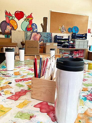 Werkraum mit Stiften und bemalbaren Bechern, im Hintergrund eine Wand mit buntem Graffiti