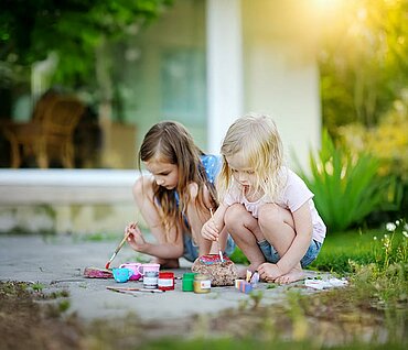 Zwei Kinder bemalen im Freien Steine mit bunten Farben
