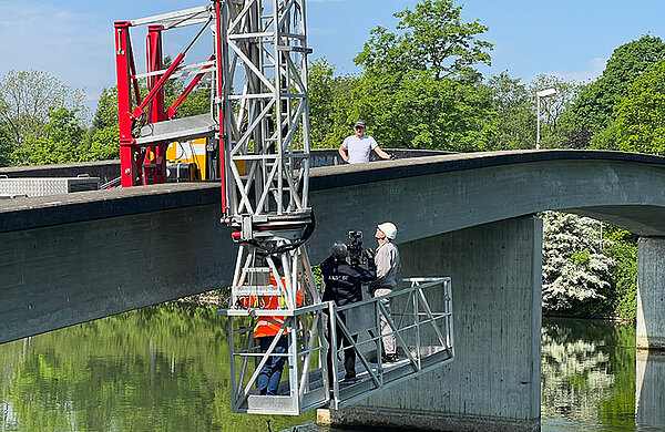 Arbeiten stehen auf einer Hebebühne, die an einer Brücke befestigt ist.