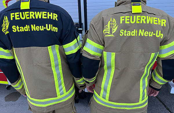 zwei Jacken von hinten, einemal sandfarbene Ausführung und einmal sandfarben mit blauen Akzenten