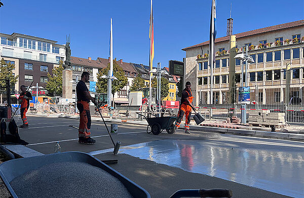 Für den mehrfarbigen Belag auf der Ludwigstraße wurde zunächst eine spezielle Grundierung aufgetragen. Anschließend erfolgte der Auftrag des farbigen Harzes und das Einstreuen von farblich passendem Granulat. Straßenbauarbeiter bringen den Belag auf der Ludwigstraße auf.