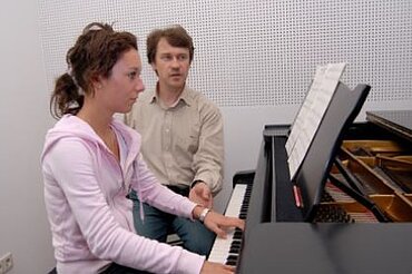 Schülerin beim Klavierspielen, daneben ihr Lehrer