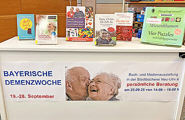 Tisch mit Büchern und einem Plakat zur bayerischen Demenzwoche im September