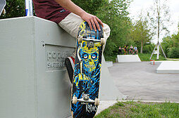 Ein Skateboard, im Hintergrund der Skateplatz in Pfuhl